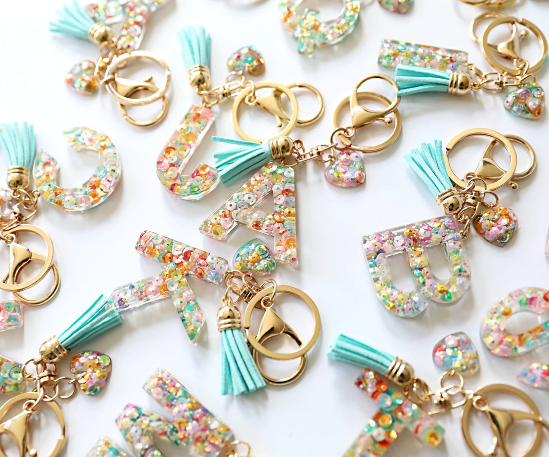 Handcrafted resin key ring with tassel and personalised initial, attached to a stylish handbag, showcasing its colourful, lightweight, and durable design.